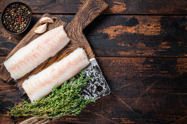 生鳕鱼里脊排在木板上，用切肉刀切。深色木制背景。前视图。本空间图片下载