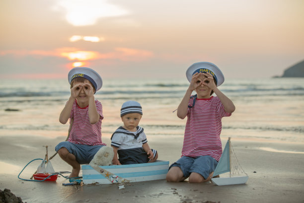 水手宝宝，可爱的孩子，在沙滩上玩木船，鱼和鱼竿在日落图片下载