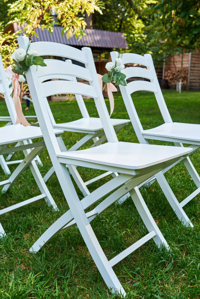 白色婚礼椅与鲜花在每一边的拱门外露，复制空间。在花园的绿色草坪上为客人准备的空木椅图片下载