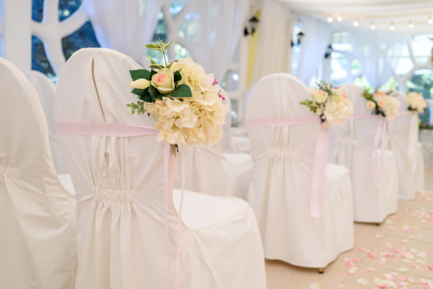 拱门两侧的白色婚礼椅上摆放着美丽的鲜花，选择性的聚焦。为婚礼上的客人空着白布椅子，自由空间图片下载
