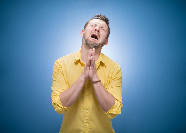 哭泣失望的年轻人请求原谅蓝色背景，穿着黄色衬衫。悲伤的家伙抬头看。罪的概念图片下载