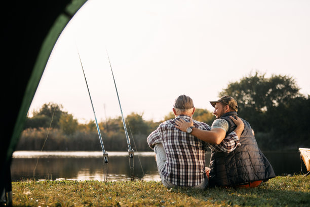 拥抱的父子在湖边露营钓鱼的后视图。图片下载