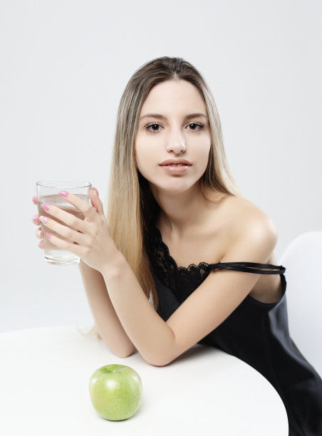 漂亮的女孩穿着睡衣，手里拿着一个绿苹果和一杯水图片下载