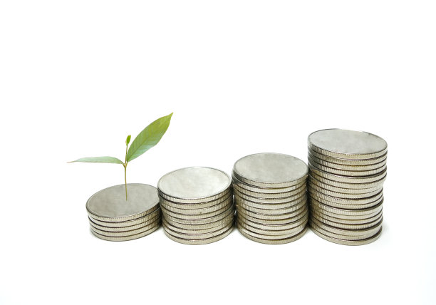 银色的金属硬币堆着绿色的小树。白色背景图片下载