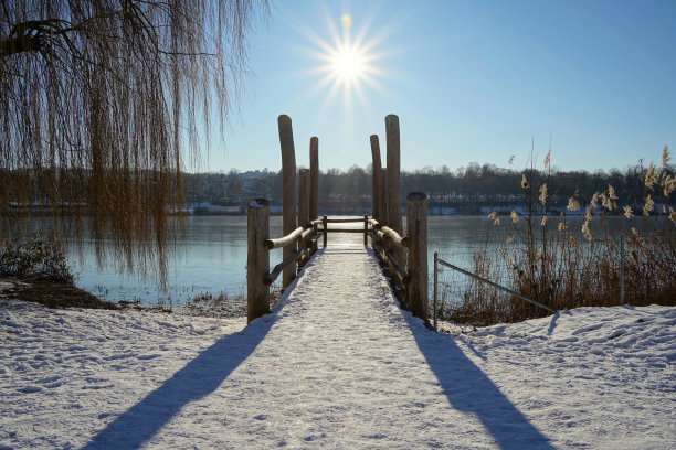 码头上还挂着白雪皑皑的码头，通向阳光下冰封的湖面。垂柳和信条在两侧。蓝色的天空。木结构的长影子。深刻的观点。图片下载