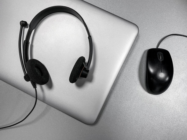 灰色笔记本电脑，带麦克风的耳机，灰色闪亮表面上的黑色鼠标。隔离中的远程教育概念。图片下载