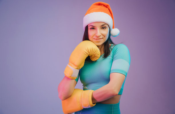 近距离照片强壮的女运动员在拳击手套和圣诞帽，拳击手摆姿势。在霓虹灯的渐变工作室背景上孤立。漂亮的白人女子在练习。图片下载