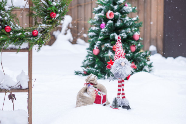 下雪的手工小矮人在红白色的衣服与礼物袋装饰圣诞树背景在冬天的时候在院子里图片下载