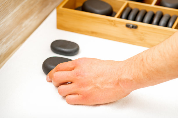 按摩师的手从水疗沙龙的桌子上取下黑色的按摩石。图片下载