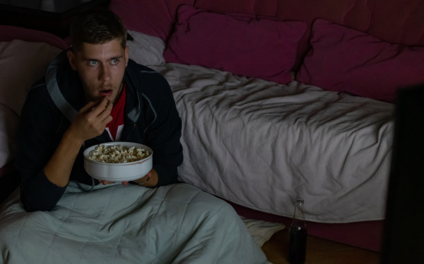 少年坐在自己房间的地板上，在黑暗中看电影，吃着爆米花喝着苏打水，享受着他的电影之夜。图片下载