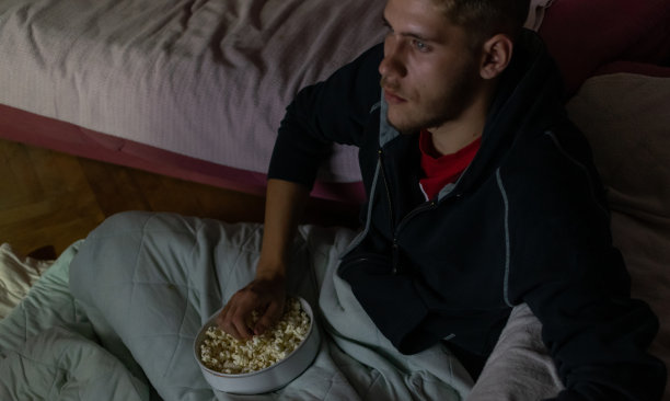 少年坐在自己房间的地板上，在黑暗中看电影，吃着爆米花喝着苏打水，享受着他的电影之夜。图片下载