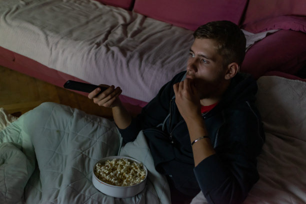 少年坐在自己房间的地板上，在黑暗中看电影，吃着爆米花喝着苏打水，享受着他的电影之夜。图片下载