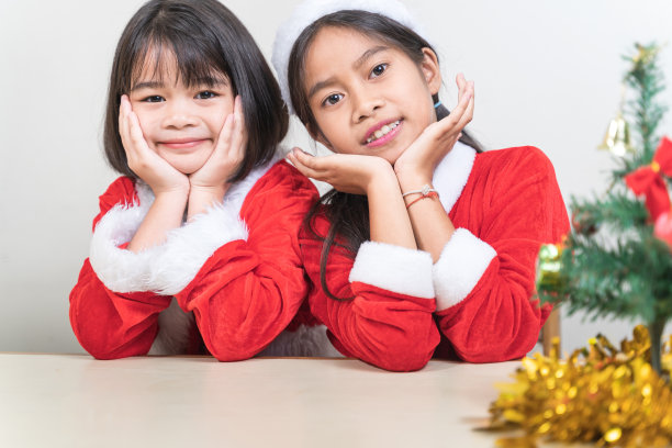 两个亚洲小女孩穿着红色的圣诞老人套装在家里庆祝圣诞节。圣诞假期概念股票照片图片下载