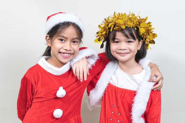 两个亚洲小女孩穿着红色的圣诞老人套装在家里庆祝圣诞节。圣诞假期概念股票照片图片下载