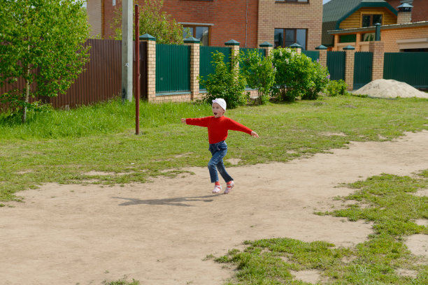 在一户人家的院子里，一个穿着红衣服的孩子伸开双臂，微笑着跑来跑去图片下载