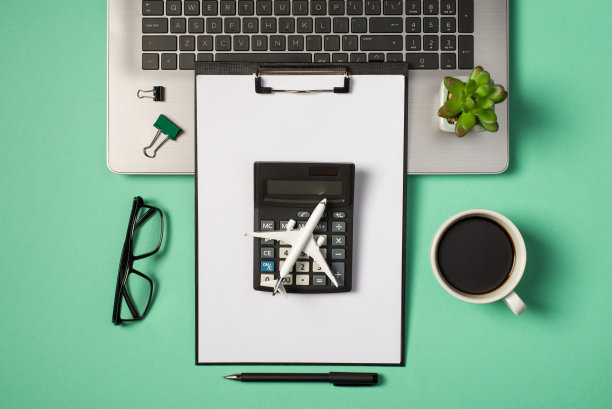 顶视图照片的绿色和黑色的夹夹植物在笔记本电脑键盘，眼镜，杯子，饮料，钢笔平面模型，计算器和黑色的剪贴板文件夹在孤立的蓝绿色背景图片下载