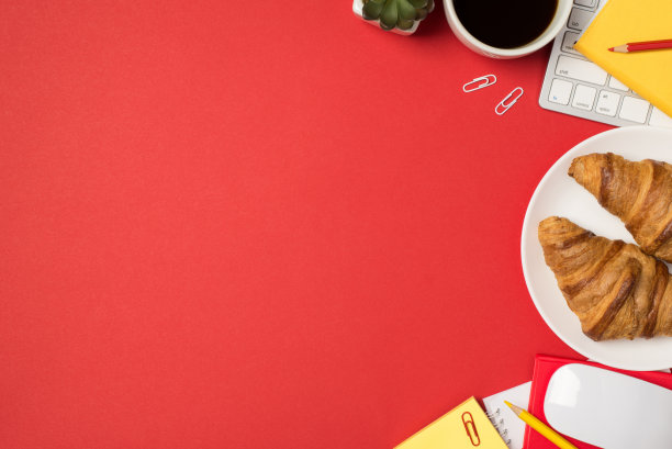 顶部视图的工作空间的照片，键盘，鼠标，黄色的便利贴，回形针种植红色铅笔规划者，咖啡，盘子和两个新鲜的羊角面包与copyspace孤立的红色背景图片下载
