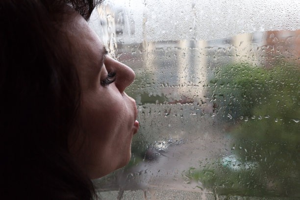一个悲伤的女人用她的嘴唇在一扇被雨打湿的窗户上吹着气。秋的概念忧郁忧郁图片下载