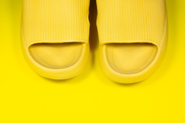 黄色背景上的黄色夏日拖鞋。一双室内鞋。极简主义创造性的照片。图片下载