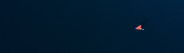 意大利撒丁岛，阳光明媚的日子里，一艘红色的帆船在蓝色的海面上航行，令人惊叹的鸟瞰图。图片下载