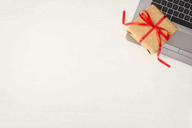 顶视图照片米色小礼品盒红色蝴蝶结笔记本电脑上孤立的白色木桌背景与copyspace图片下载