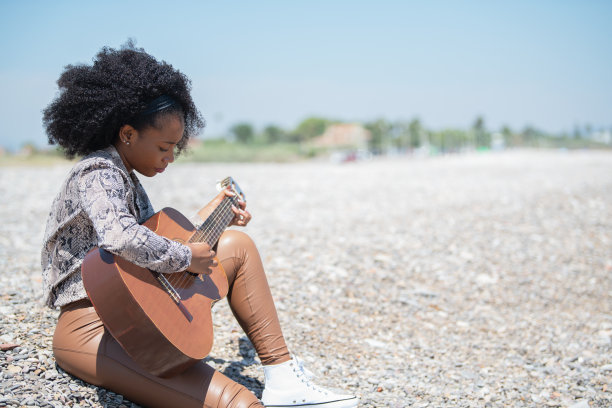 放松的年轻女子坐在碎石的地面上，在空中弹奏着她的原声吉他图片下载
