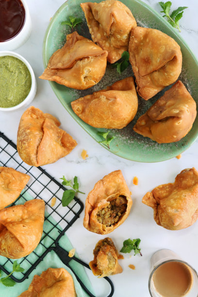 图片:绿色的油炸萨莫萨饼，少了一口，里面塞满了五香土豆，豌豆和肉，冷却架，绿色的平纹棉布，薄荷香菜蘸酱和芒果酸辣酱，一杯印度茶，大理石效果的背景，高架的视野图片下载