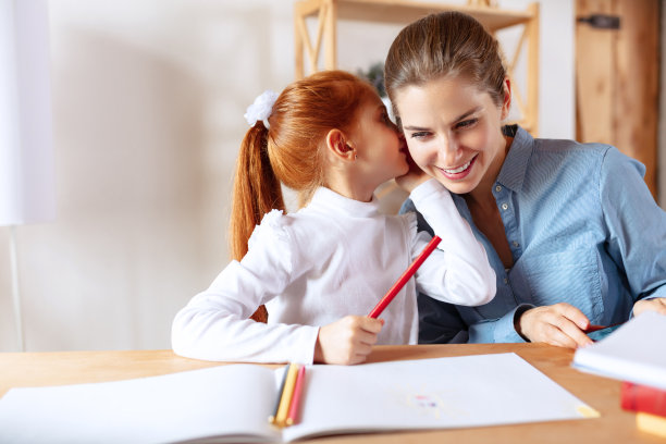 一个快乐的小女孩和她妈妈耳语的画像。一家人一起做家庭作业图片下载