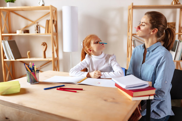 快乐的家庭。妈妈和女儿一起做作业，玩得很开心，还做鬼脸图片下载