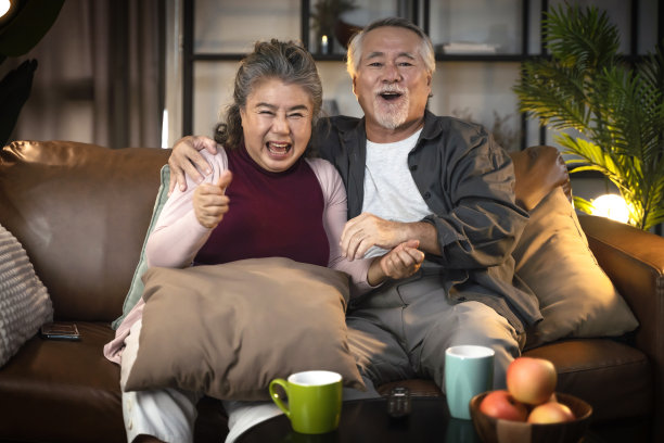 老退休的老亚洲夫妇在家里看电视，老成熟的亚洲夫妇一起在客厅的沙发沙发上欢笑胜利的体育比赛助威活动图片下载