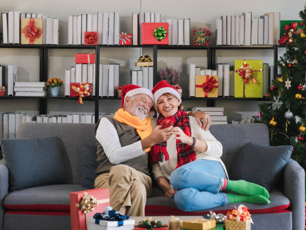 快乐的白人年长的男子拥抱和给他心爱的妻子圣诞礼物，而放松坐在沙发上的一天在家里。圣诞节和新年庆祝活动。图片下载