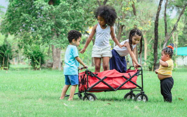 可爱的混血小孩子们在户外的绿色公园里拉着一辆红色的小车玩耍。教育、多样性和团队精神。图片下载