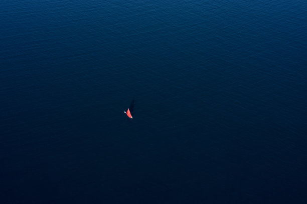 意大利撒丁岛，阳光明媚的日子里，一艘红色的帆船在蓝色的海面上航行，令人惊叹的鸟瞰图。图片下载