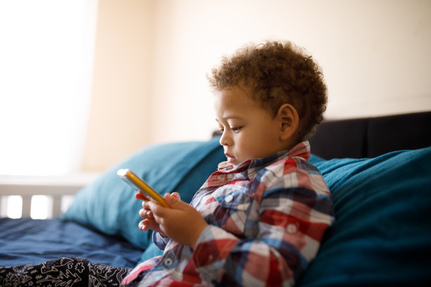 可爱的孩子在床上玩智能手机图片下载