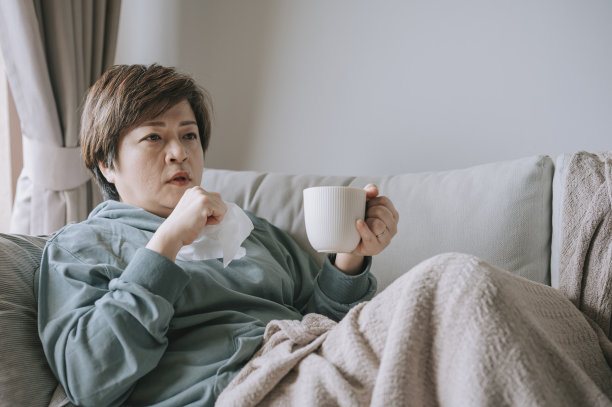 亚洲华人中年妇女用纸巾咳嗽不舒服，坐在沙发上休息图片下载