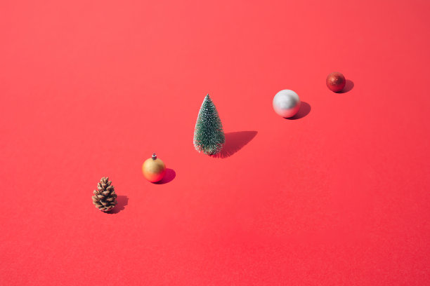 安排新年和圣诞树与金色，银色，红色的小玩意和棕色松果在红色粉彩背景。模式。图片下载