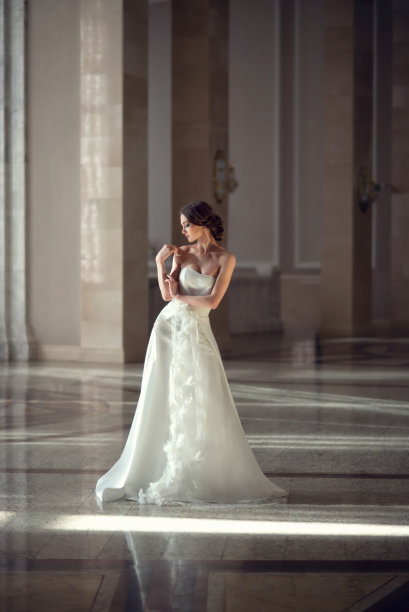 年轻脆弱的黑发女孩。新娘穿着奢华的婚纱在别致的室内与美丽的阳光从窗户婚礼发型和化妆。婚礼盐，美容院照片图片下载