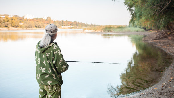 河岸边老大，一个人拿着钓竿钓鱼，美丽的大自然，秋天。一位老人休息并热爱他的爱好。积极健康的生活方式，户外运动。图片下载