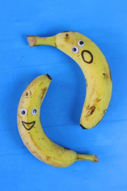 有趣的特写图像，卡通面孔在成熟的香蕉上，有大眼睛和嘴巴，笑脸和震惊的脸，蓝色背景，升高的视野，儿童健康饮食，幽默的概念图片下载