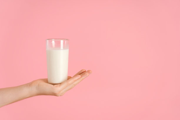 粉红色背景上有一只手，手里拿着一杯牛奶。摊开的手掌里放着一杯乳制品图片下载