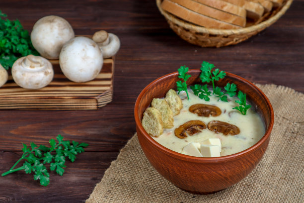 深色木桌上放着香槟酒汤，里面有融化的奶酪、欧芹和面包块，背景是蘑菇和面包。图片下载