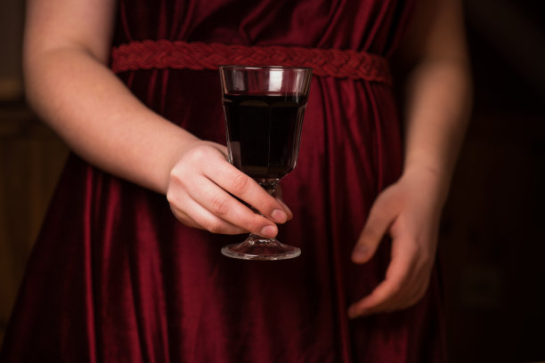 一杯红酒放在红色天鹅绒裙子上。浪漫晚餐的概念。一杯酒在一个年轻女孩的手中。红丝绒和激情在一张照片图片下载