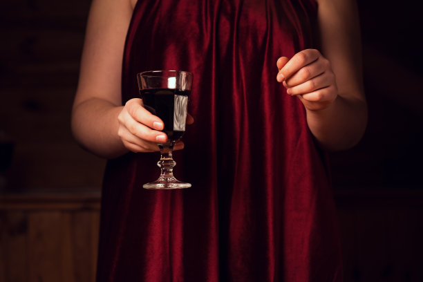 一杯红酒放在红色天鹅绒裙子上。浪漫晚餐的概念。一杯酒在一个年轻女孩的手中。红丝绒和激情在一张照片图片下载