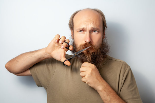 一名英俊的成年男子用剪刀剪着胡子，带着遗憾的目光移开了视线。图片下载