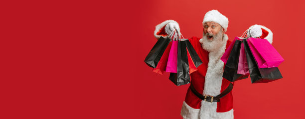 穿着圣诞老人服装的老人的裁剪肖像和假日许多购物袋在红色背景上。假日销售。摩天观景轮图片下载
