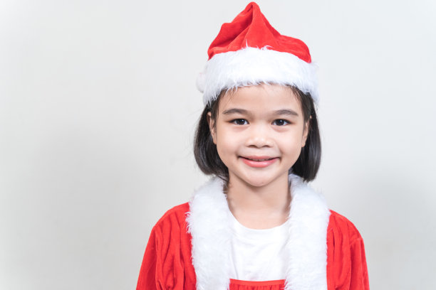 一个可爱的亚洲小女孩在圣诞夜穿着红色的圣诞老人服装装饰圣诞树。泰国圣诞假期概念库存照片图片下载