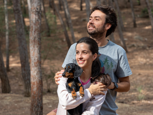 秋天的森林里，一对快乐的白种人夫妇带着他们的迷你腊肠狗微笑图片下载