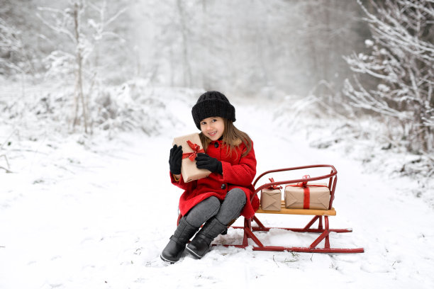 一个戴着针织帽子的女孩正拿着圣诞礼物坐在雪橇上图片下载