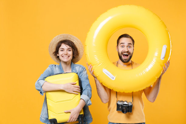 震惊的年轻游客夫妇朋友男孩女孩穿着夏装，帽子孤立在黄色背景上。周末出国旅游的乘客。航空旅行的概念。拿好充气环箱。图片下载
