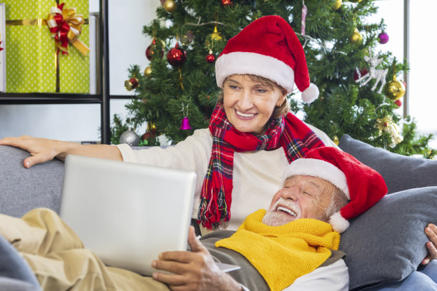 白种人老夫妇在装饰好的圣诞树上戴着红色的圣诞老人帽，用笔记本电脑与家人视频通话，一起快乐地庆祝圣诞节图片下载